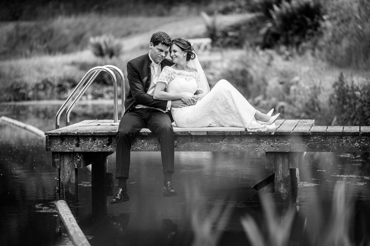 Braut und Bräutigam sitzen am Teich der Bärenmühle im Kellerwald