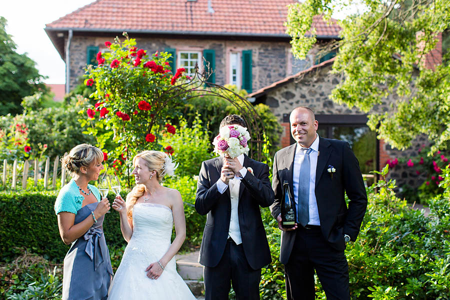Sekt und Blumenstrauß mit Braut und Bräutigam und Freunden